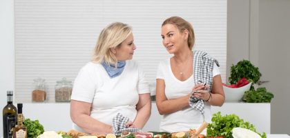 Two women in a kitchen preparing fresh vegetables and cheese with olive oil and spices.