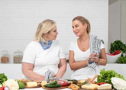 Two women in a kitchen preparing fresh vegetables and cheese with olive oil and spices.