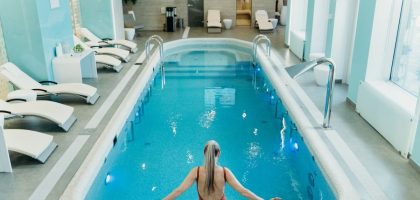 A woman in a red swimsuit prepares to enter an elegant indoor pool at a luxurious spa.