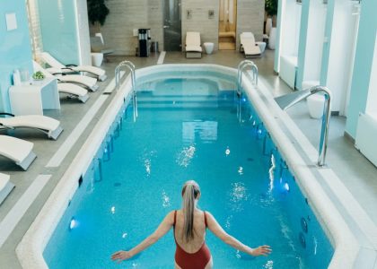A woman in a red swimsuit prepares to enter an elegant indoor pool at a luxurious spa.
